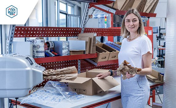 PaperBubble erzeugt Papierpolster, die in die Kartonage an einem Packtisch mit diversen Schutz- und Polstermaterialien, wie z. B. Luftpolsterfolie, zum Schutz des Produkt beigelegt werden.