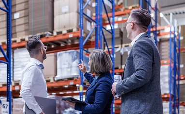 Ein Verpackungsberater steht mit Kunden in eine Logistik-Halle.