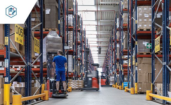 In einer Logistikhalle werden Paletten und Kartonagen mit Gabelstapler transportiert.