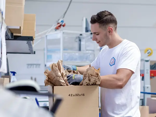 Zwei Logistikmitarbeiter*innen verpacken Produkte in einen Karton.