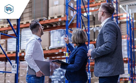 In einer Logistikhalle unterhalten sich 3 Mitarbeite*innen über die Lagerung verschiedener Produkte.