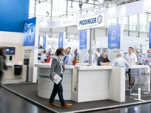 In einer Messehalle ist ein Stand von PRODINGER zu sehen, auf dem Besucher von Mitarbeitern beraten werden.