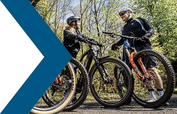 In einem Waldstück stehen mehrere Mountainbike-Fahrer*innen und unterhalten sich.