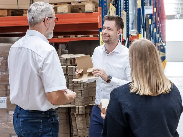 Beratungsgespräch vor einem Hochregallager in einem Logistikzentrum über die richtige Verpackungslösung für Kostensenkung und Prozessoptimierung rund um Transportverpackung