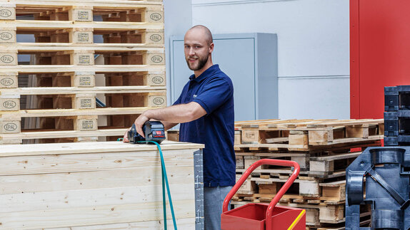 Lager-Mitarbeiter sichert Waren auf einer Palette mit einem Umreifungsband.