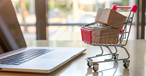 Ein Miniatur-Einkaufswagen steht neben einem aufgeklappten Laptop.