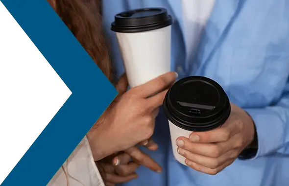 Nachaufnahme auf die Hände zweier Personen, die jeweils einen Pappbecher mit Kunststoffdeckel in der Hand halten.