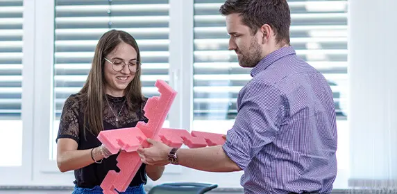 Zwei Mitarbeiter der Verpackungsentwicklung von PRODINGER Verpackung prüfen ein Formteil aus Schaumstoff.