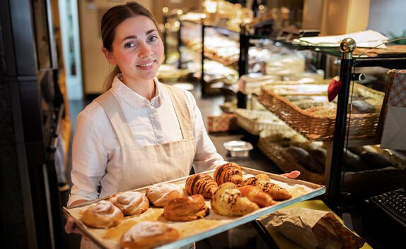 Eine Bäckerin hält ein Tablett mit verschiedene Croissants und anderem Gebäck in die Kamera.