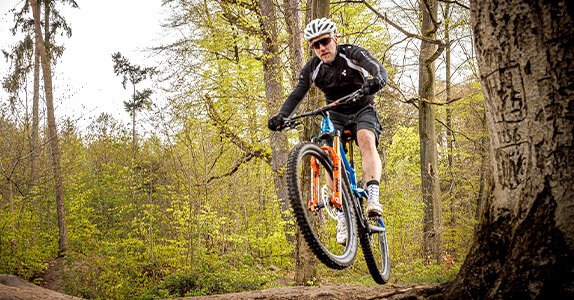 In einem Waldgebiet springt ein Mountainbiker mit seinem Rad.