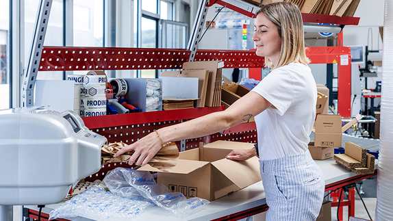PaperBubble erzeugt Papierpolster, die in die Kartonage an einem Packtisch mit diversen Schutz- und Polstermaterialien, wie z. B. Luftpolsterfolie, zum Schutz des Produkt beigelegt werden.
