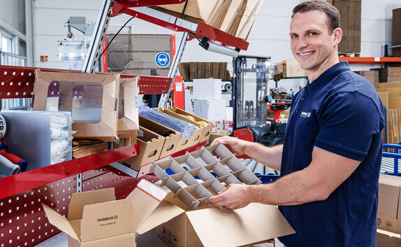 Ein Mitarbeiter im Logistikzentrum verpackt Produkte in Kartonagen.