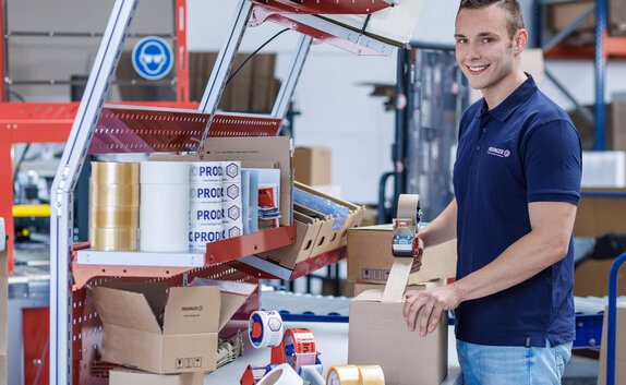 Mitarbeiter im Logistikzentrum klebt einen Karton mit einem Paketabroller zu.