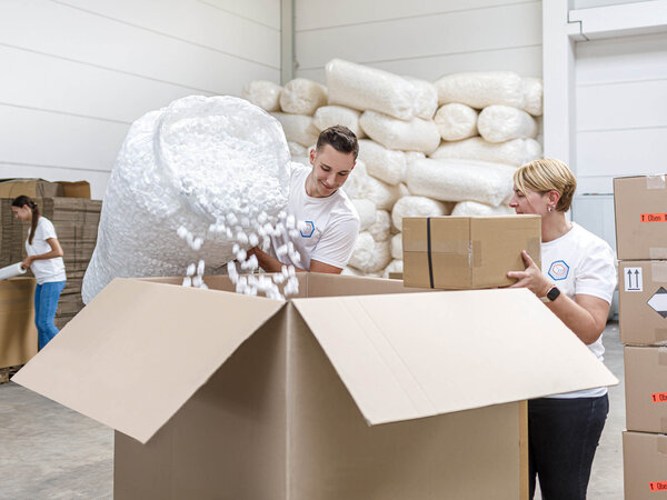 Logistikmitarbeiter packen ein großes Paket und schützen das Produkt mit Packmitteln wie Styropor.