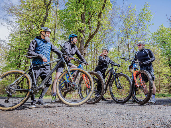 4 Radfahrer stehen zusammen im Wald und besprechen Ihre Tour.