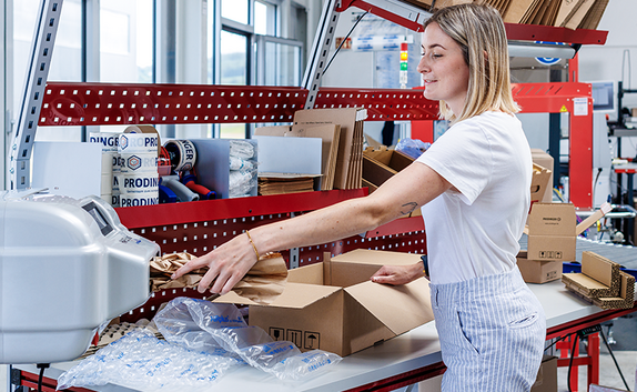 PaperBubble erzeugt Papierpolster, die in die Kartonage an einem Packtisch mit diversen Schutz- und Polstermaterialien, wie z. B. Luftpolsterfolie, zum Schutz des Produkt beigelegt werden.