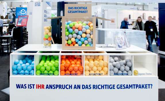 Auf dem Messestand von PRODINGER Verpackung symbolisieren mehrere, mit bunten Stressbällen gefüllte Kästen, das richtige Gesamtpaket für einen Kunden.